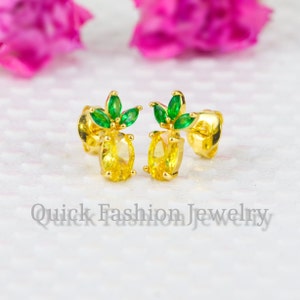 Op de afbeelding: Een paar gouden ananas oorbellen met gele en groene zirkonia stenen.