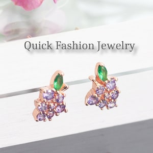 May include: A pair of rose gold earrings with a grape design. The grapes are made of purple and clear rhinestones and the leaves are green.