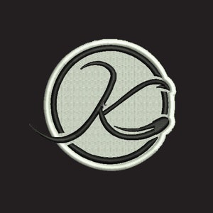 May include: A black and white embroidered patch with a stylized letter "K" inside a white circle with a black outline.