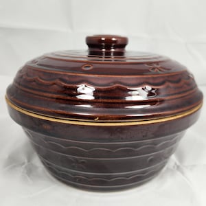 May include: A brown ceramic casserole dish with a lid. The dish has a scalloped edge and a floral design. The lid has a knob on top.