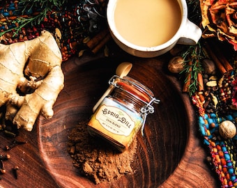 May include: A warm, inviting image featuring a cup of chai tea, a jar of Sprig & Dill Chai Blend, and various spices like cinnamon sticks and cloves. The scene is set on a wooden tray with dried flowers and greenery.