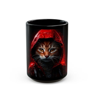 May include: A black ceramic mug with a colorful image of a cat wearing a red hooded jacket. The cat has orange and brown fur and yellow eyes.