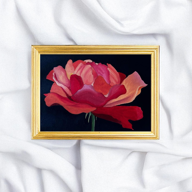 May include: A framed painting of a red rose against a dark background. The rose features layers of red and pink petals. The rectangular frame is gold-coloured. The painting is set against a white fabric background.