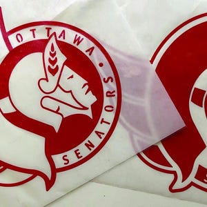 K&ouml;nnte beinhalten: Zwei rote und wei&szlig;e Ottawa Senators Logo-Aufkleber. Das Logo zeigt einen stilisierten Gladiatorenkopf in einem kreisf&ouml;rmigen Design mit den Worten "OTTAWA SENATORS". Die Aufkleber befinden sich auf wei&szlig;em Hintergrund.