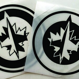 K&ouml;nnte beinhalten: Zwei kreisf&ouml;rmige schwarz-wei&szlig;e Aufkleber mit einem stilisierten Ahornblatt und einem Kompassrosen-Design. Die Aufkleber haben einen schwarzen Rand und befinden sich auf wei&szlig;em Hintergrund. Das Design ist ein Logo.