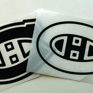 K&ouml;nnte beinhalten: Zwei schwarz-wei&szlig;e Aufkleber mit dem Logo der Eishockeymannschaft Montreal Canadiens. Das Logo ist ein stilisiertes "C" mit einem "H" darin und zwei kleinen Quadraten. Die Aufkleber befinden sich auf wei&szlig;em Hintergrund.