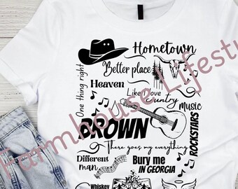 May include: A white t-shirt with black text and graphics. The text includes "Hometown", "Heaven", "Like Love Country Music", "BROWN", "There goes my everything", "Different man", "Bury me in Georgia", "Whiskey Sour", and "Thank god".