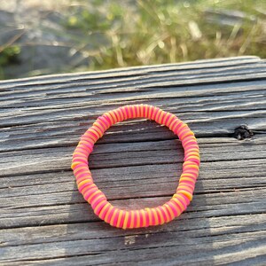 May include: A pink and yellow rubber bracelet made of stacked rings.
