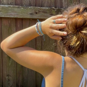 May include: A woman wearing a denim tank top with a white strap and a blue and white beaded bracelet on her wrist.