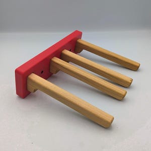 May include: A red wooden rack with four natural wood dowels extending from it. The rack is painted a vibrant red, and the dowels are smooth and evenly spaced. The design is simple and modern, suitable for various organizational purposes.