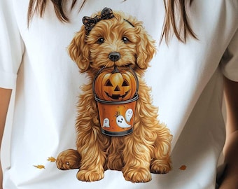 May include: White t-shirt with a graphic of a brown and white dog holding a pumpkin. The dog is wearing a black bow.