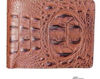 May include: A brown bi-fold wallet with a crocodile skin texture. The wallet has a detailed pattern with a central oval design and a small crocodile logo in the bottom right corner. The color is a warm, reddish-brown.
