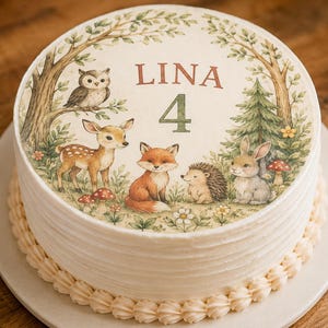Könnte beinhalten: Ein runder, weiß glasierter Kuchen mit einem runden essbaren Aufleger, der eine Waldszene zeigt. Die Illustration umfasst eine Eule, ein Reh, einen Fuchs, einen Igel und einen Hasen, mit dem Text LINA und der Zahl 4 in der Mitte.