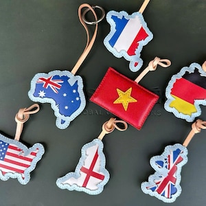 May include: Leather keyrings in the shape of various countries, including the United States, Australia, France, Germany, and the United Kingdom. Each keyring features the country's flag design and a light blue border. The keyrings are attached to leather straps.