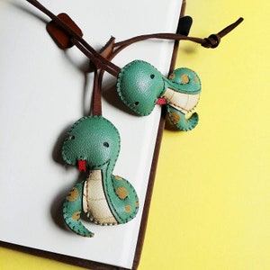 Peut inclure: Deux porte-clés en cuir vert en forme de serpent avec des lanières en cuir marron. Les serpents ont des bouches rouges et des ventres blancs.