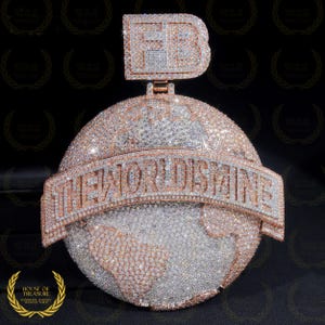 Könnte beinhalten: Ein Anhänger aus Gold und Diamanten mit einem Globus mit den Worten "The World Is Mine" und einem "FB" Initial-Anhänger.