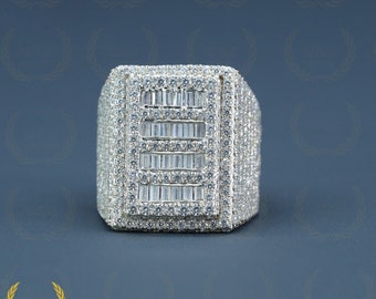 May include: A silver ring with a large square-shaped setting featuring a row of baguette-cut diamonds surrounded by smaller round diamonds.