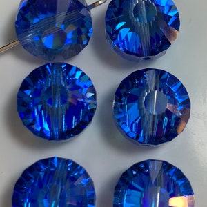 May include: Six blue faceted glass beads with a hole through the center. The beads are round and have a shiny, iridescent finish.