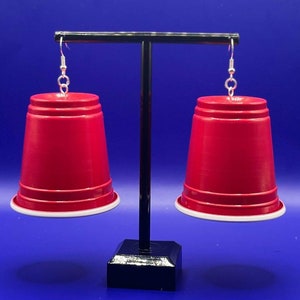 May include: A pair of red plastic cup earrings with silver hooks. The cups have a white rim.