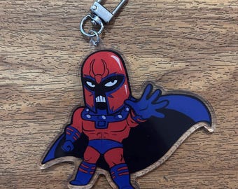 May include: A red and blue cartoon character keychain with a silver clip. The character is wearing a red helmet with horns and a blue cape. The character is holding out its right hand.