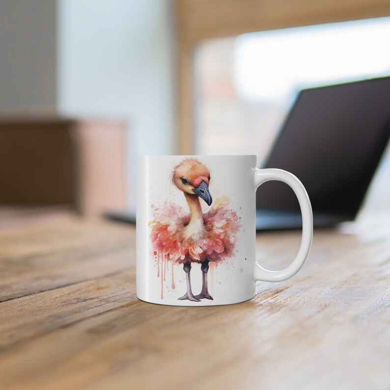 May include: White ceramic mug with a watercolor illustration of a pink flamingo with a long neck and a pink beak. The flamingo is standing on one leg and has its wings spread out.
