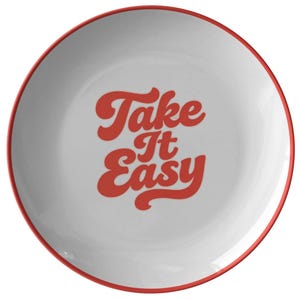 Puede incluir: Plato de cer&aacute;mica blanco con borde rojo. El plato presenta la frase "Take It Easy" en una fuente retro roja. El dise&ntilde;o es simple y limpio, adecuado para el uso diario.