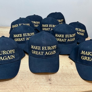 Op de afbeelding: Een groep van negen zwarte baseballpetten met gouden borduurwerk. Alle petten hebben dezelfde tekst: "Make Europe Great Again".