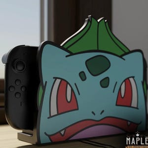 Puede incluir: Soporte personalizado para consola Nintendo Switch con diseño de Bulbasaur en azul claro, verde y rojo. El logotipo de Maple 3D Printing es visible en la parte inferior.