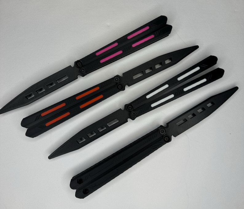 May include: Three black butterfly knives with different colored accents. The first knife has pink accents, the second has orange accents, and the third has white accents.