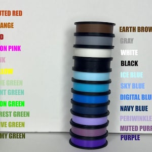 May include: A collection of 18 spools of filament for 3D printing, arranged in two columns. The left column features shades of green, yellow, pink, and red. The right column features shades of blue, purple, brown, gray, and white.