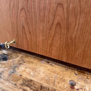 May include: Close-up of a wooden cabinet with a keyhole and a decorative brass key. The cabinet is made of reddish-brown wood with visible grain patterns. The key is attached to the cabinet's side.