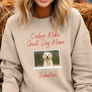 May include: A beige sweatshirt with the text "Coders Make Great Dog Moms" and a picture of a golden retriever in a laptop screen. The text "Sebastian" is below the laptop image.