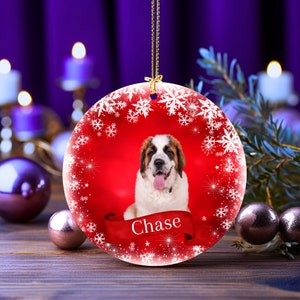 May include: A round Christmas ornament featuring a Saint Bernard dog with a red background and white snowflake border. The dog's name, "Chase," is displayed on a red banner. The ornament hangs from a gold chain.
