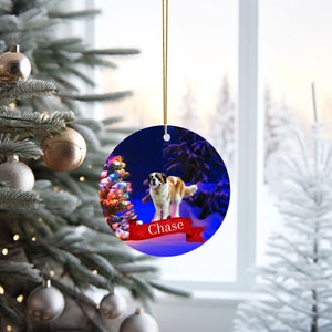 May include: Round Christmas ornament featuring a Saint Bernard dog in a snowy winter scene. The dog is brown and white, standing on a red banner with the name "Chase". A decorated Christmas tree and snow-covered trees are in the background.