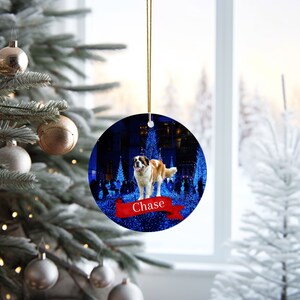 May include: Round Christmas ornament featuring a Saint Bernard dog with brown and white fur, set against a backdrop of blue lights. A red banner with the name "Chase" is at the bottom. The ornament hangs from a gold string.