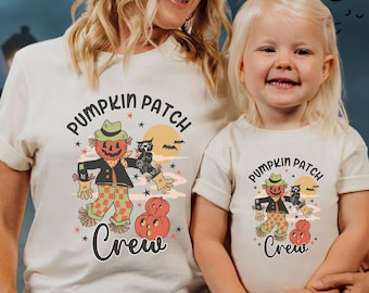 May include: Two matching cream t-shirts with a Halloween graphic. The design includes a scarecrow with a pumpkin head, an owl, and the words "Pumpkin Patch Crew".