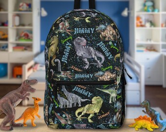 May include: A black backpack with a dinosaur print and the name "JIMMY" repeated throughout. The backpack has a zipper closure and adjustable straps.
