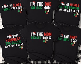 May include: Black t-shirts with Christmas-themed text in red and green. The shirts have phrases like "I'm the Dad, go ask Mom" and "I'm the Baby, the real boss." Each shirt has a Santa hat and ornament graphic.