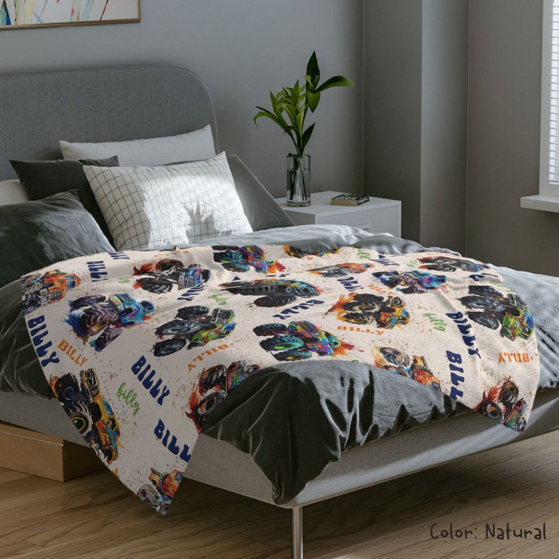 May include: A soft, beige fleece blanket with a repeating pattern of monster trucks. The trucks are blue, green, and orange with flames and the name "Billy" printed on them.