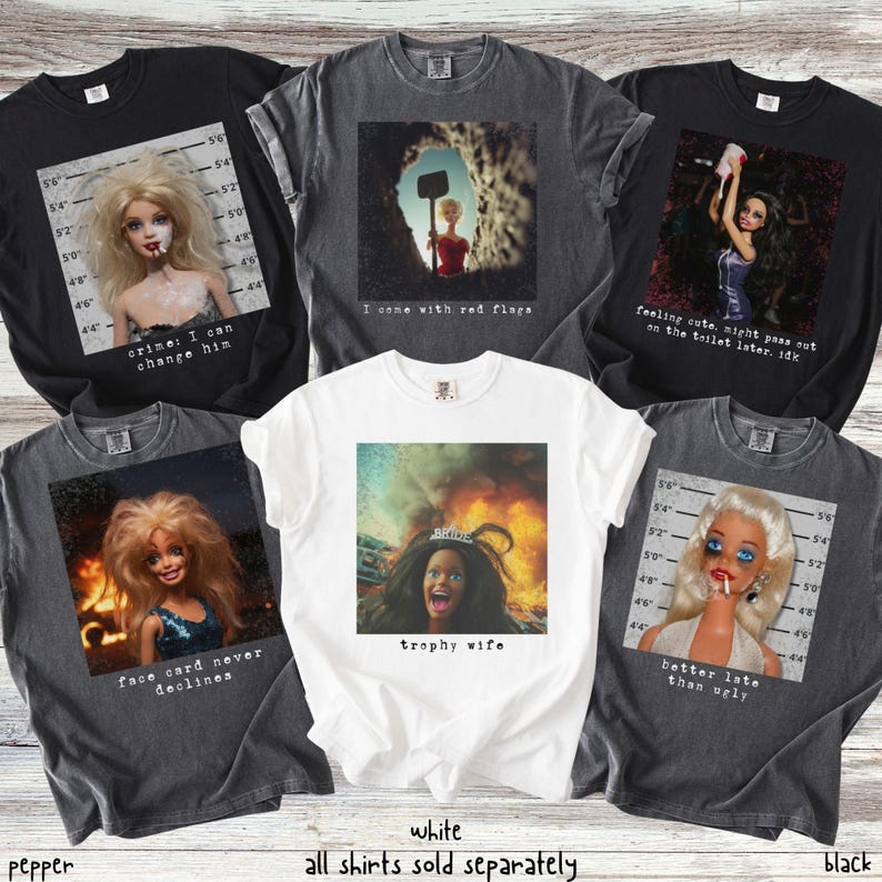 May include: A collection of black, white, and pepper-colored t-shirts. Each shirt features a unique graphic design with text and a doll image. The text includes phrases like "crime: I can change him" and "trophy wife."