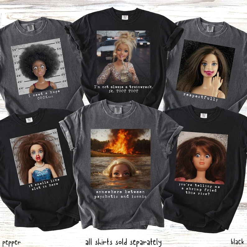 May include: A collection of black and gray graphic t-shirts. Each shirt features a doll image with text. The text includes phrases like "I need a huge cock...", "I'm not always a trainwreck", and "somewhere between psychotic and iconic."