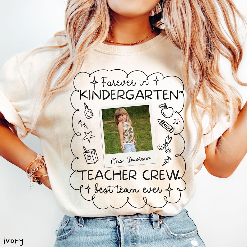 May include: Ivory-colored sweatshirt with a photo of a young girl and the words "Forever in Kindergarten" and "Teacher Crew". The design includes school-themed illustrations like an apple, pencil, and scissors. The text "best team ever" is also included.