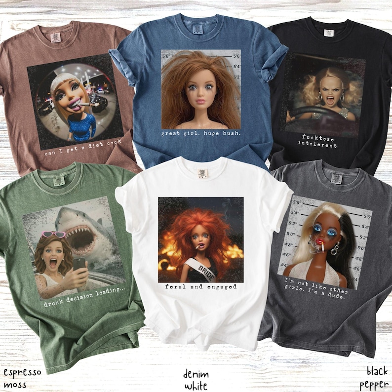 May include: Collection of six graphic t-shirts in various colors, including espresso moss, denim white, and black pepper. Each shirt features a unique image of a doll or a person with text. The text includes phrases like "great girl, huge bush" and "feral and engaged."