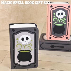 Puede incluir: Una caja de regalo Magic Spell Book gris con un diseño de calavera y caldero. La caja tiene un interior blanco y está decorada con estrellas. La imagen también incluye el texto "INSTANT DOWNLOAD" y "SVG CUT FILES FOR DIE CUT MACHINES".