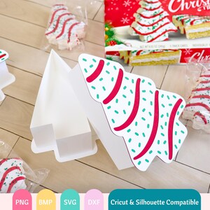 Puede incluir: Una caja de cart&oacute;n blanca en forma de &aacute;rbol de Navidad con un dise&ntilde;o de patr&oacute;n rojo y verde. La caja est&aacute; abierta y contiene tres peque&ntilde;os pasteles de &aacute;rbol de Navidad. Los pasteles est&aacute;n decorados con glaseado rojo y verde y chispas. La caja es compatible con las m&aacute;quinas de corte Cricut y Silhouette.