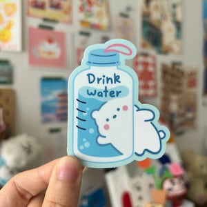 Puede incluir: Una pegatina azul y blanca con un oso polar de dibujos animados bebiendo agua de una botella. La botella tiene el texto "Drink Water".
