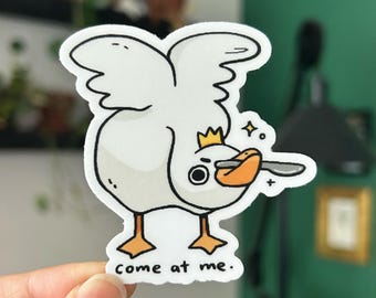 Könnte beinhalten: Weißer Aufkleber mit einer Cartoon-Gans, die eine Krone trägt und ein Messer hält. Die Gans hat einen überraschten Ausdruck und sagt "komm her".