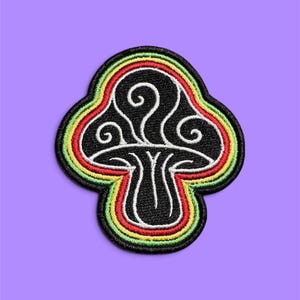 May include: An embroidered patch shaped like a mushroom with a black background and white line art detailing. The mushroom cap features swirling white patterns, and the entire design is bordered by concentric rings of red, yellow, and green thread.