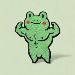 Könnte beinhalten: Gestickter Aufnäher mit einem muskulösen grünen Frosch, der seine Arme anspannt. Der Frosch hat schwarze Umrisse, rote Wangen und ein kleines Kreuz auf der Brust. Auf hellgrünem Hintergrund.