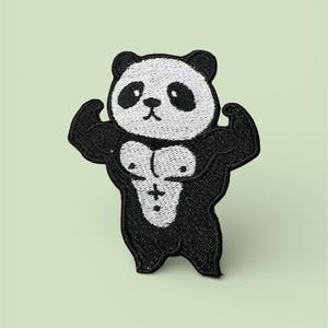 Puede incluir: Parche bordado con un oso panda musculoso flexionando los brazos. El panda es blanco y negro con pecho y brazos definidos, sobre un fondo verde claro. El parche está diseñado para planchar o coser sobre tela.